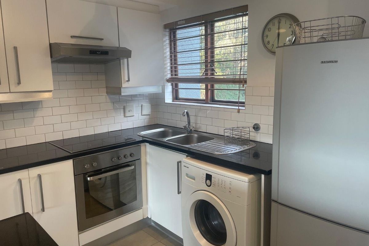 A functional kitchen featuring white cabinetry, subway tile backsplash, dark countertops, and integrated appliances including an oven, hob, and extractor fan.