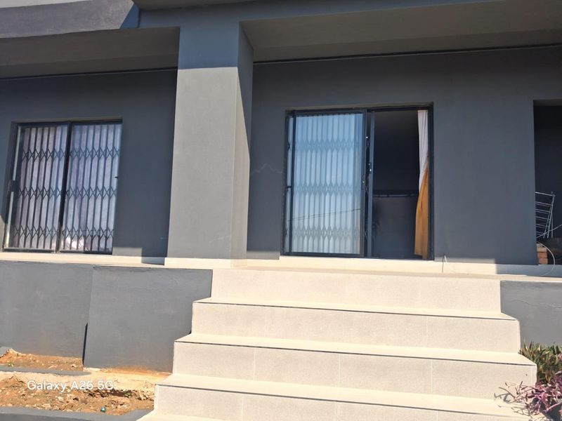 A rear exterior view of the property featuring a tiled staircase leading to sliding glass doors with security gates and dark grey exterior walls.