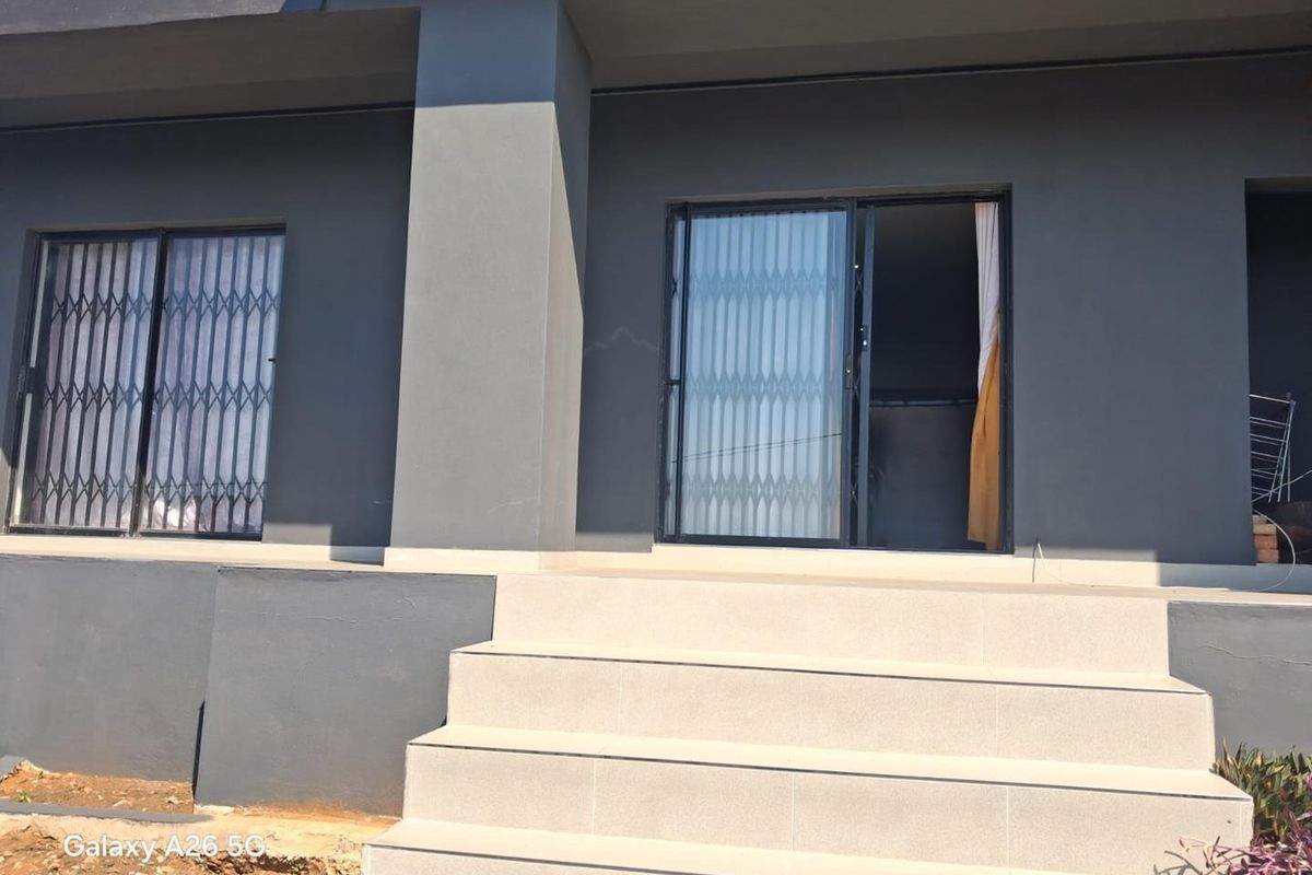 A rear exterior view of the property featuring a tiled staircase leading to sliding glass doors with security gates and dark grey exterior walls.