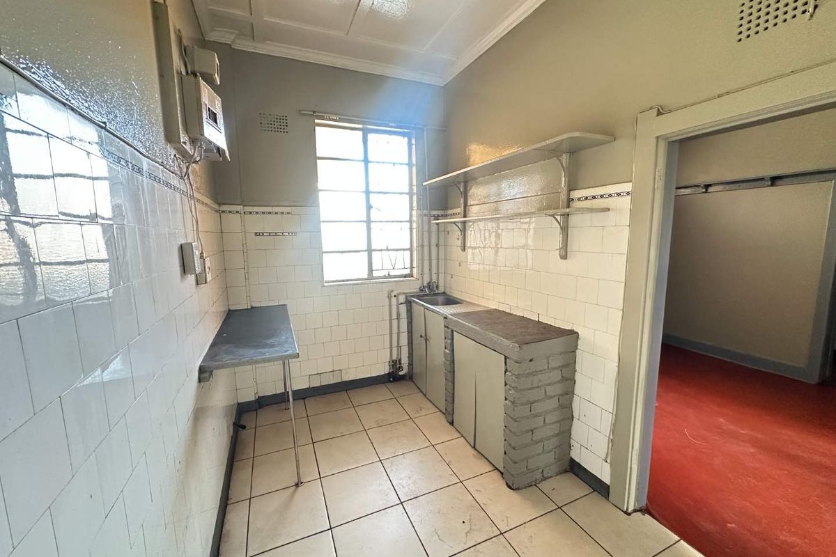 A functional, empty kitchen area featuring tiled flooring, ceramic wall tiling, a stainless steel sink, and built-in brick cabinetry with metal shelving.