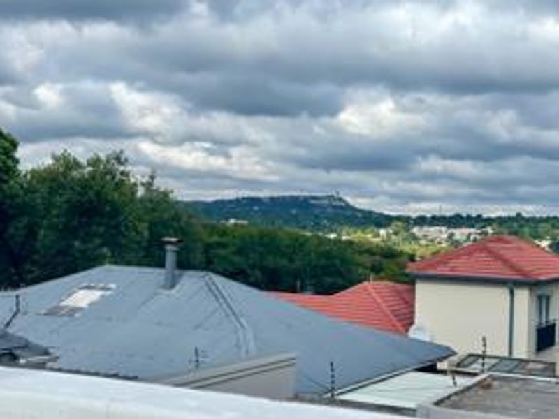 An elevated view overlooking neighbouring rooftops and surrounding landscape under a cloudy sky.