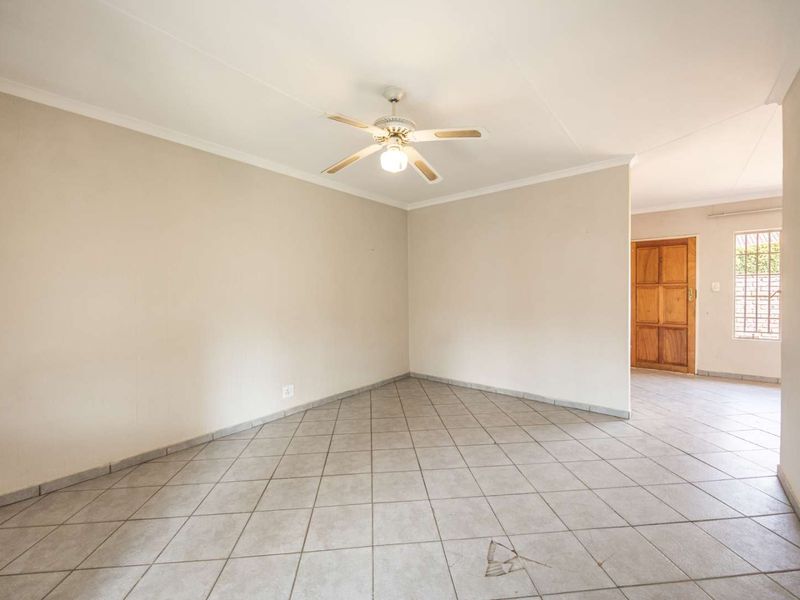 An empty, open-plan living area featuring neutral walls, tiled flooring, and a ceiling fan, with a view toward an adjacent entrance area.