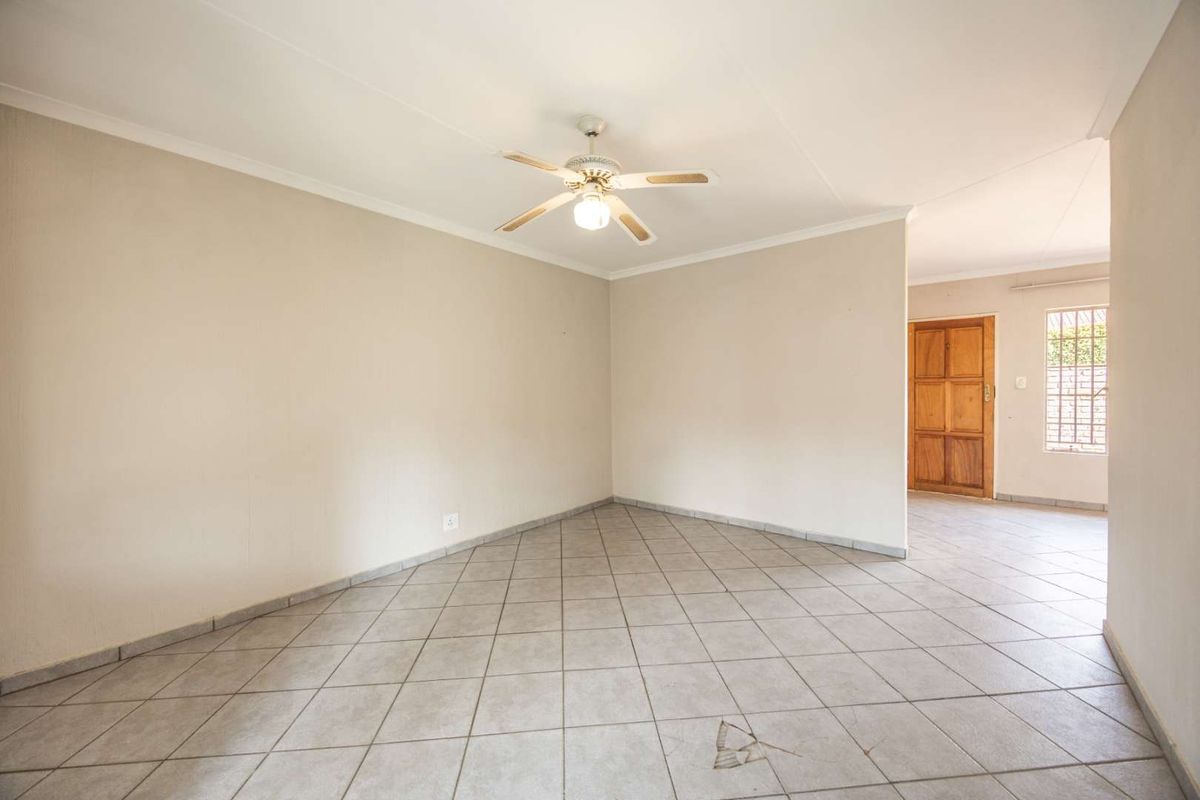 An empty, open-plan living area featuring neutral walls, tiled flooring, and a ceiling fan, with a view toward an adjacent entrance area.