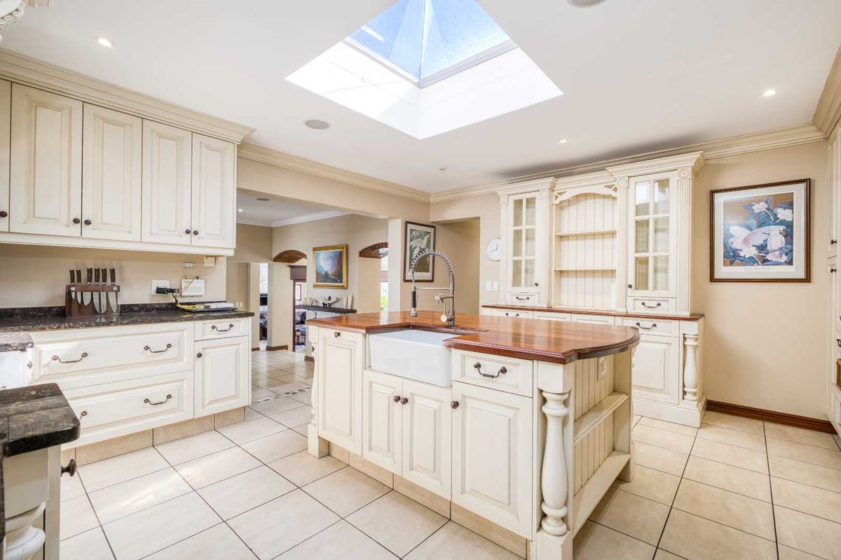 A bright, traditional-style kitchen featuring a central island with a farmhouse sink, timber countertops, ample built-in cabinetry, and a large overhead skylight.