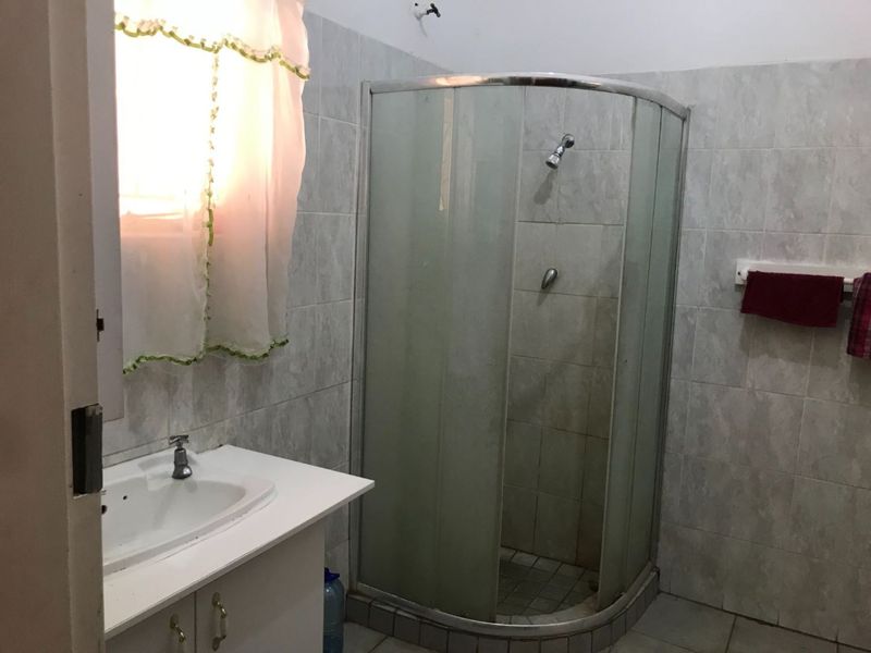 A functional bathroom featuring a corner shower enclosure, vanity basin, and neutral wall tiling.