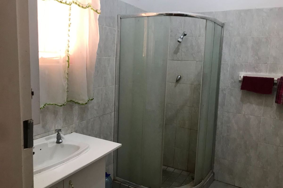 A functional bathroom featuring a corner shower enclosure, vanity basin, and neutral wall tiling.