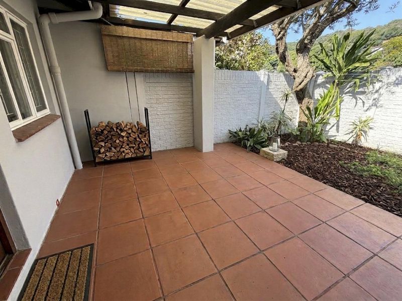 A covered outdoor patio area featuring terracotta-style floor tiles, a brick boundary wall, and direct access to a small garden space.