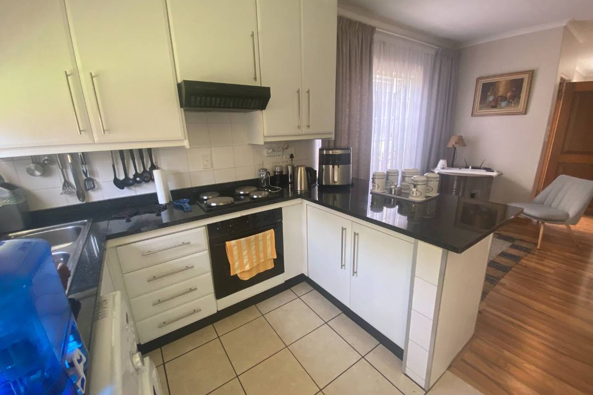 A functional kitchen featuring white cabinetry, dark granite countertops, a built-in oven, and a hob with an extractor fan, opening into a living area.