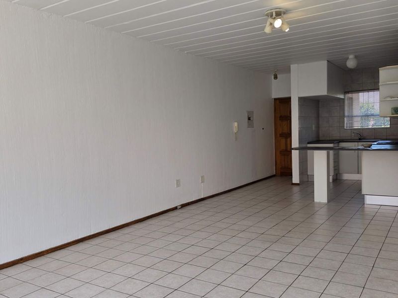 An open-plan living and kitchen area featuring tiled flooring, a breakfast bar, and functional kitchen cabinetry in a neutral, vacant space.