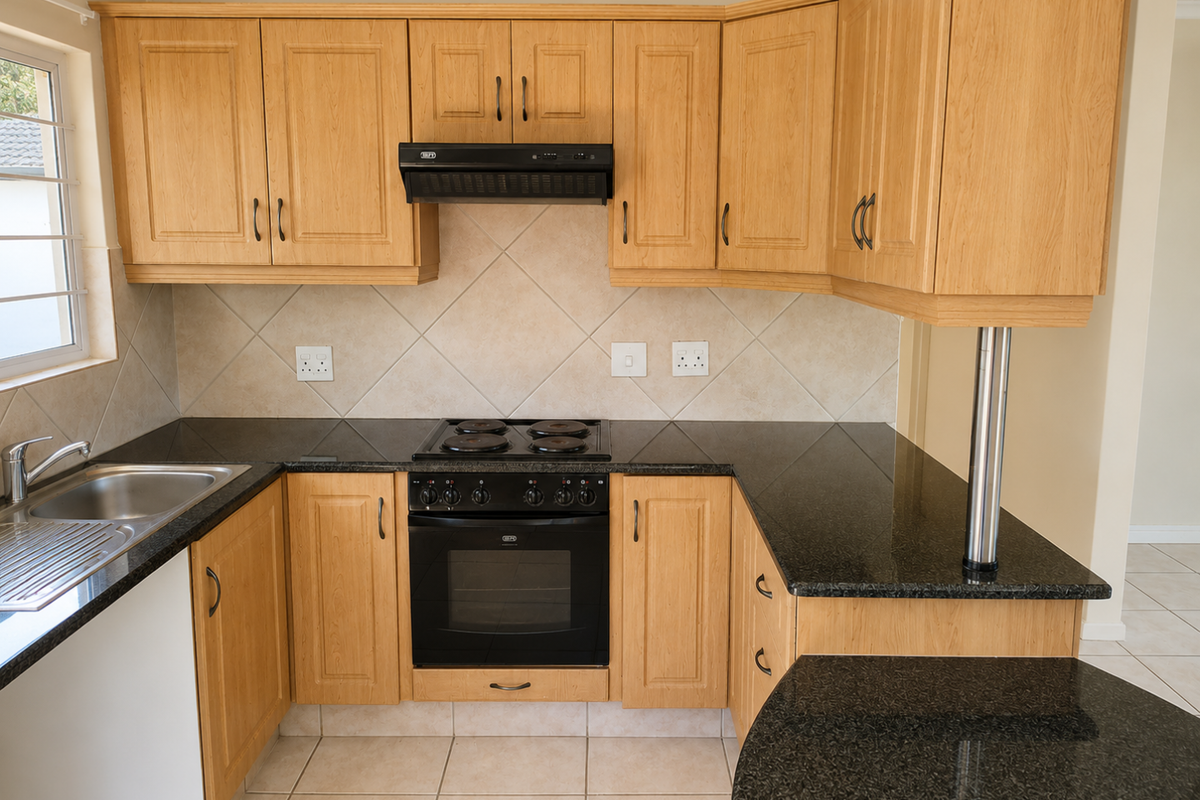 A functional kitchen featuring light wood cabinetry, dark granite countertops, a built-in oven, electric hob, and tiled finishes throughout.