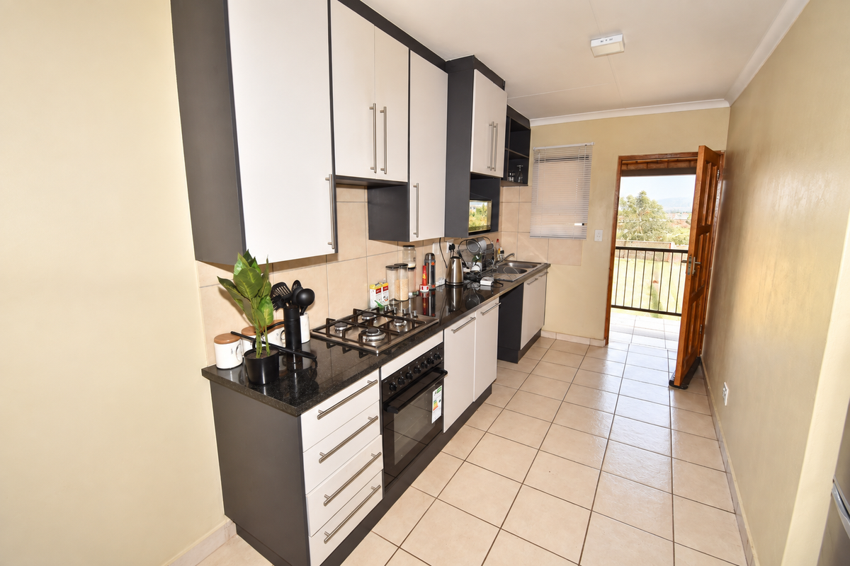 A functional kitchen featuring modern two-tone cabinetry, granite countertops, a gas hob, and direct access to an outdoor balcony area.