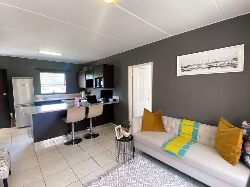 Open plan living area featuring a kitchen with dark cabinetry, a breakfast island, and tiled flooring, seamlessly connected to the lounge space.
