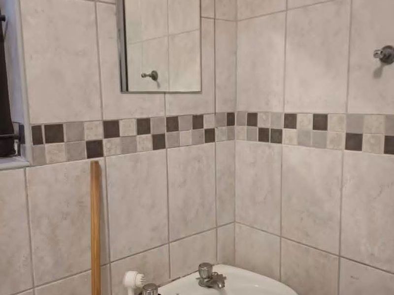A compact bathroom featuring a pedestal basin, wall-mounted mirror, and tiled walls with a decorative border.