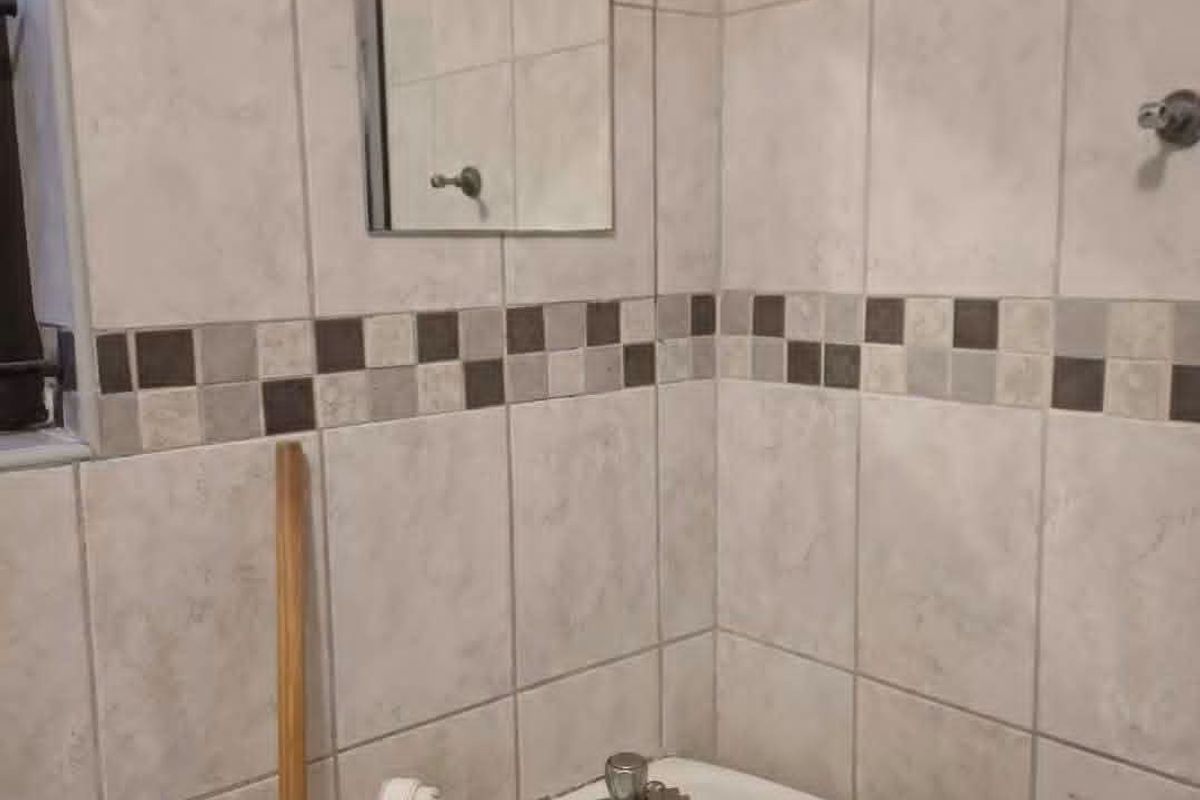 A compact bathroom featuring a pedestal basin, wall-mounted mirror, and tiled walls with a decorative border.