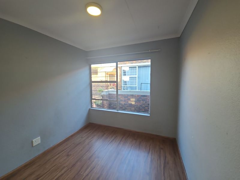 An empty bedroom featuring laminate flooring, neutral grey walls, and a window with security bars, offering a clean canvas for personalization.