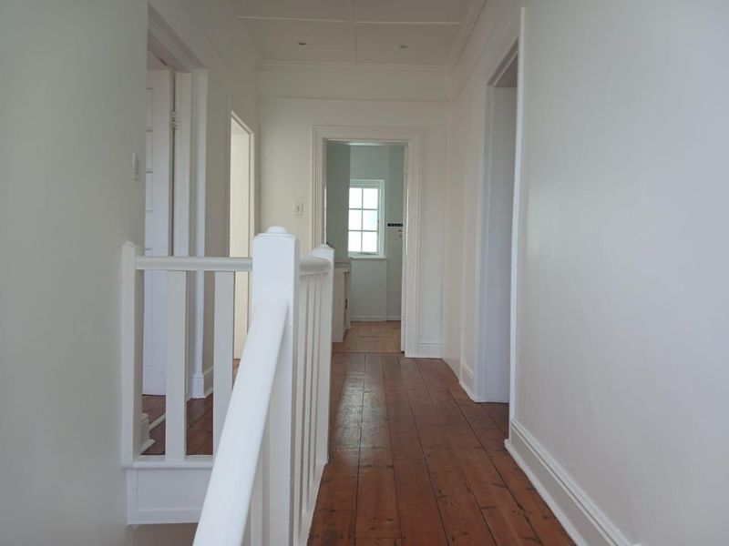 A bright, empty hallway featuring polished timber flooring and a white staircase balustrade, providing access to multiple rooms.