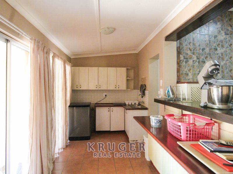 A functional scullery area featuring built-in cabinetry, a stainless steel sink, tiled backsplash, and a breakfast bar overlooking the adjacent living space.
