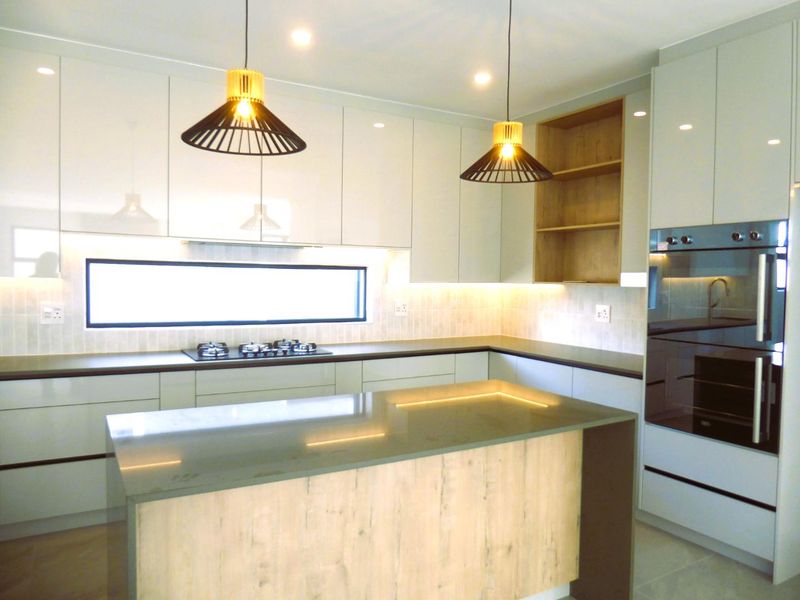 Modern kitchen featuring high-gloss cabinetry, stone countertops, a central island, integrated gas cooktop, and built-in oven with elegant under-cabinet lighting.