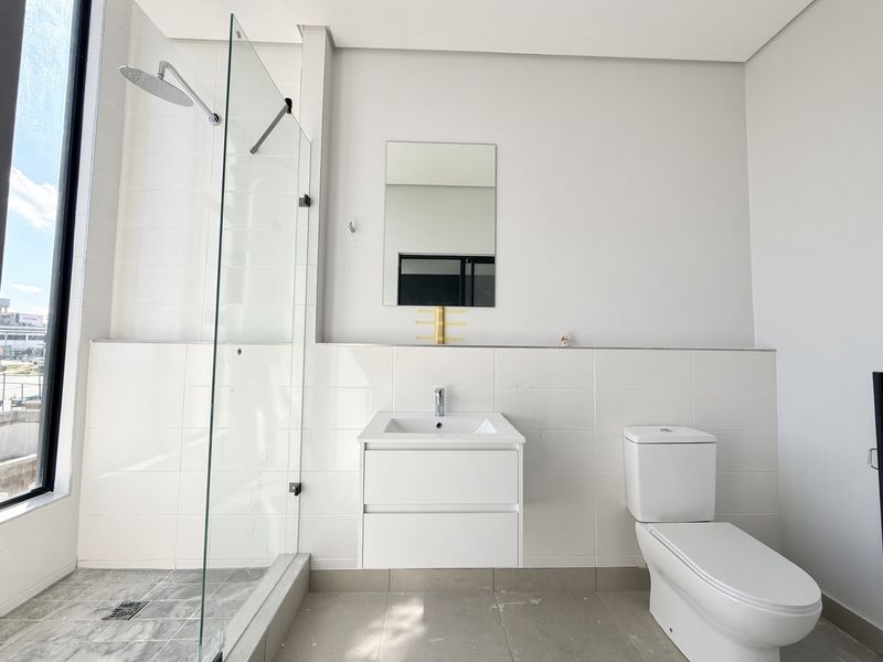 Modern bathroom featuring a glass-enclosed shower, wall-mounted vanity, and neutral tiling, offering a clean and functional space.