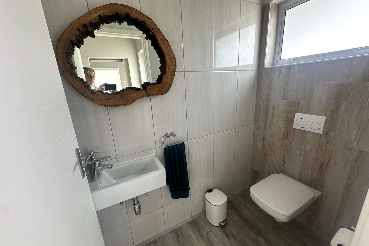 Modern guest bathroom featuring a wall-mounted toilet, sleek vanity basin, and contemporary neutral tiling with wood-look flooring.