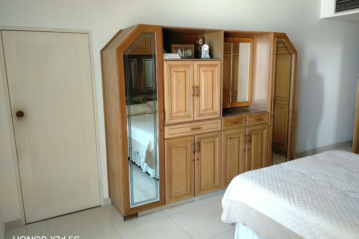 A bedroom featuring a large wooden built-in wardrobe with mirrored panels, tiled flooring, and a ceiling-mounted air conditioning vent.