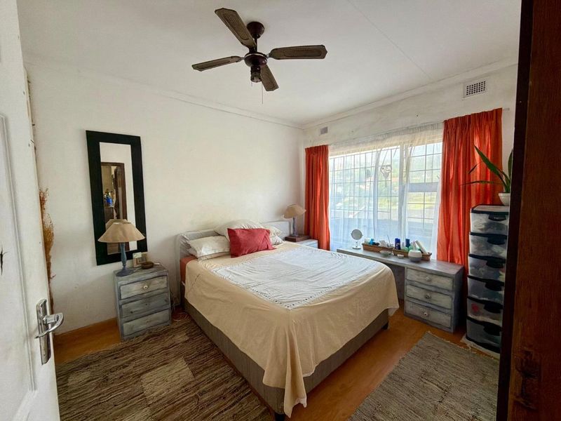 A bedroom featuring laminate flooring, a ceiling fan, and large windows with security bars, requiring cosmetic updates to improve its overall condition.