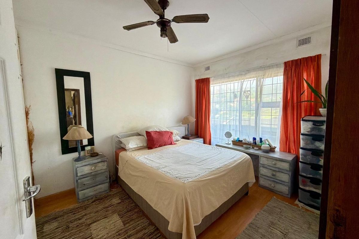 A bedroom featuring laminate flooring, a ceiling fan, and large windows with security bars, requiring cosmetic updates to improve its overall condition.