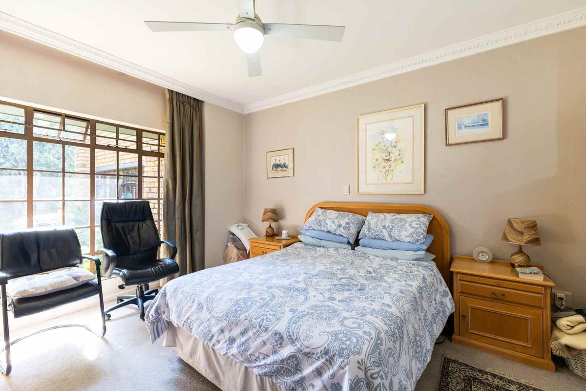 A well-lit bedroom featuring a ceiling fan, large window with natural light, and neutral wall finishes.