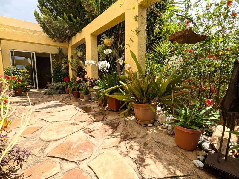 A charming outdoor patio area featuring natural stone paving and a structural concrete pergola, providing a seamless transition to the interior living space.