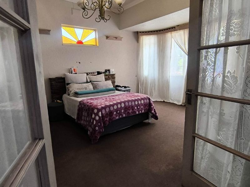 Spacious bedroom featuring an ornate ceiling rose, stained glass accent window, and classic french door entry, offering a unique architectural character.