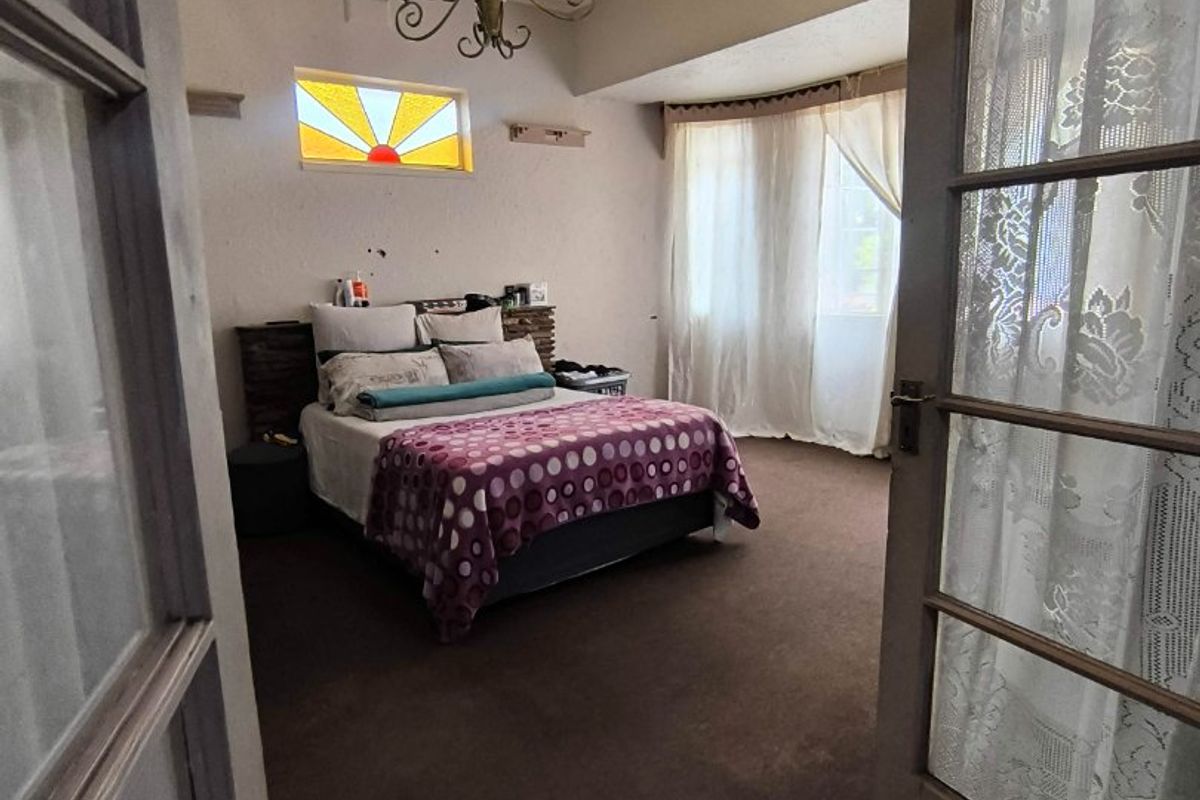 Spacious bedroom featuring an ornate ceiling rose, stained glass accent window, and classic french door entry, offering a unique architectural character.