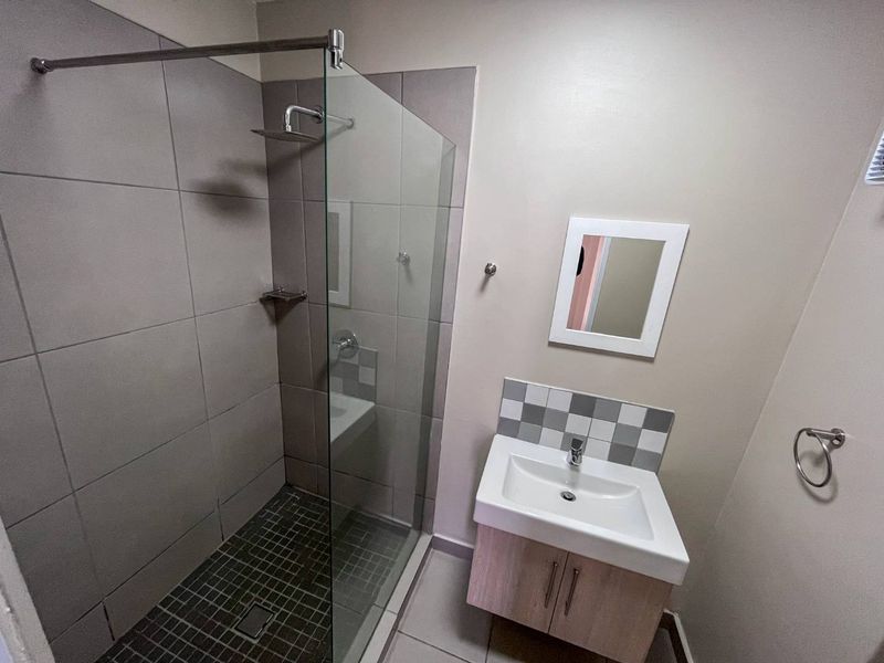 Modern bathroom featuring a glass-enclosed shower with tiled flooring and a vanity cabinet with a basin.