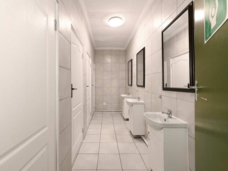 A functional communal bathroom area featuring multiple vanity basins, tiled walls and flooring, and several access doors.