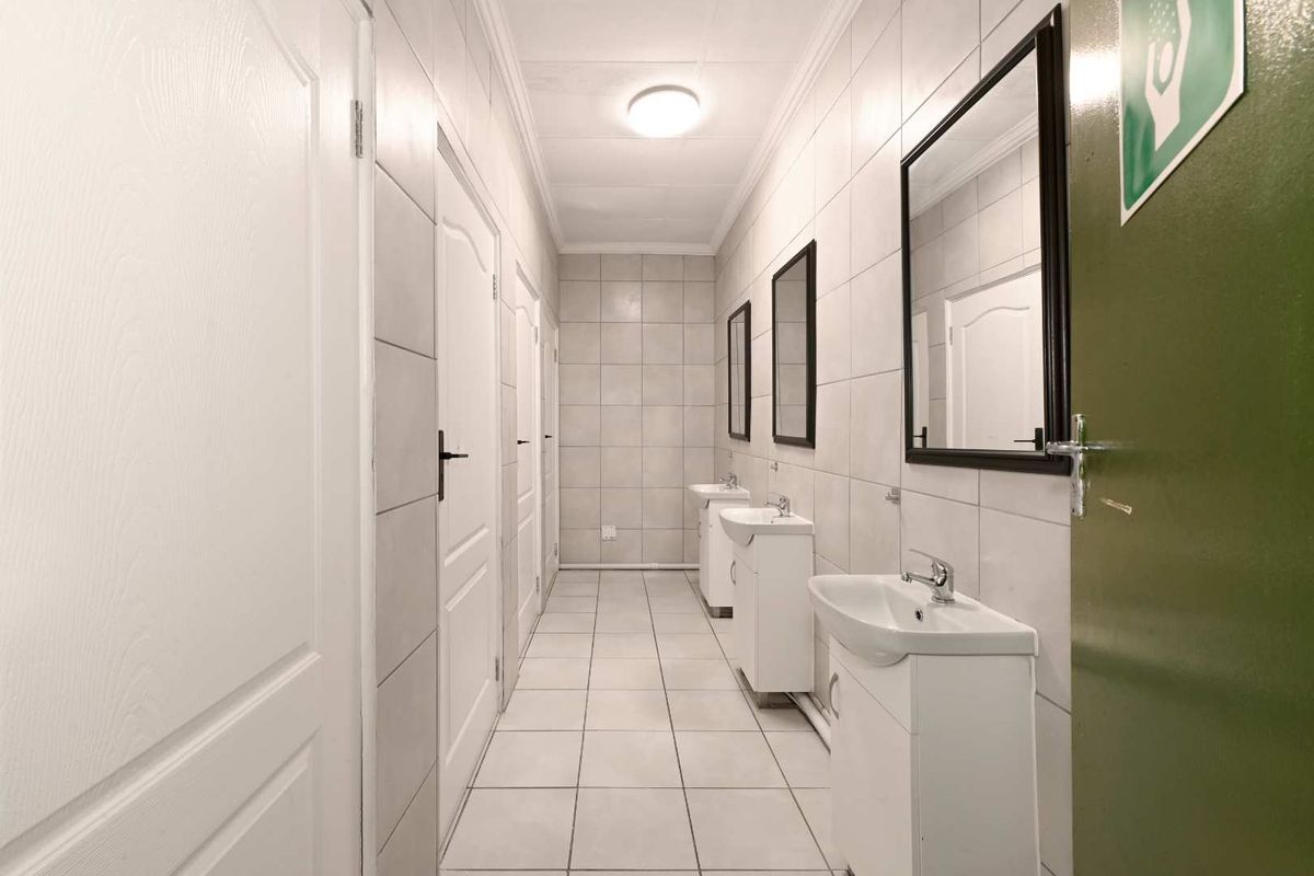 A functional communal bathroom area featuring multiple vanity basins, tiled walls and flooring, and several access doors.