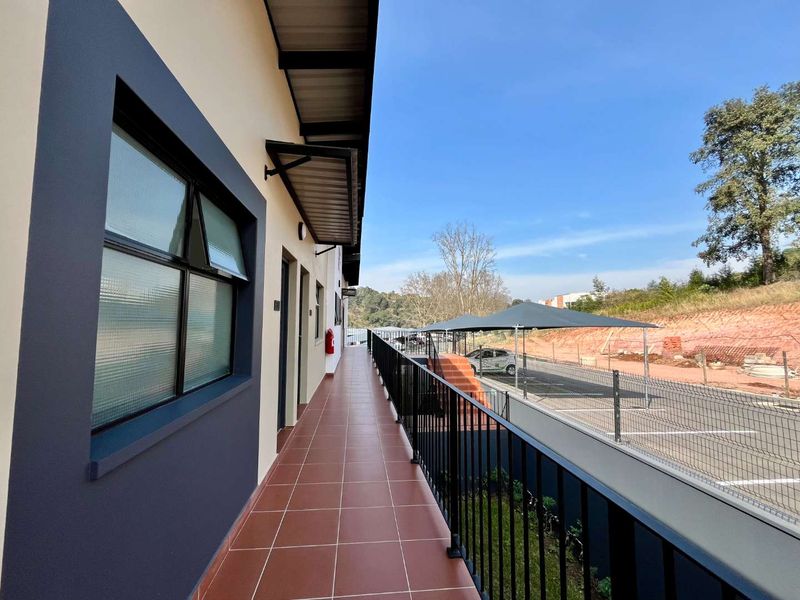 A clean, modern exterior balcony featuring tiled flooring, a protective awning, and a secure metal balustrade overlooking the parking area.
