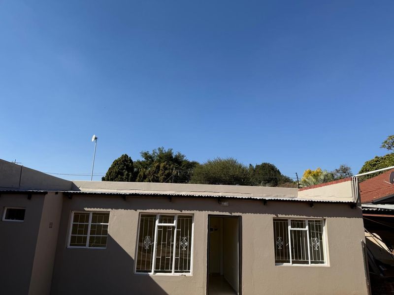 Rear exterior view of the cottage featuring a corrugated metal roof, security bars on windows, and neutral painted exterior walls.