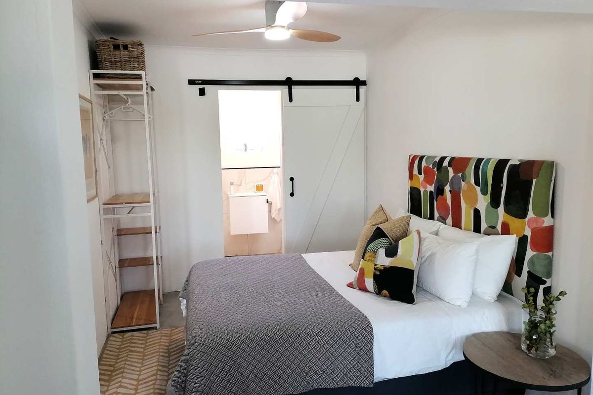 A well-lit bedroom featuring a sliding barn door leading to an en-suite bathroom and a ceiling fan.