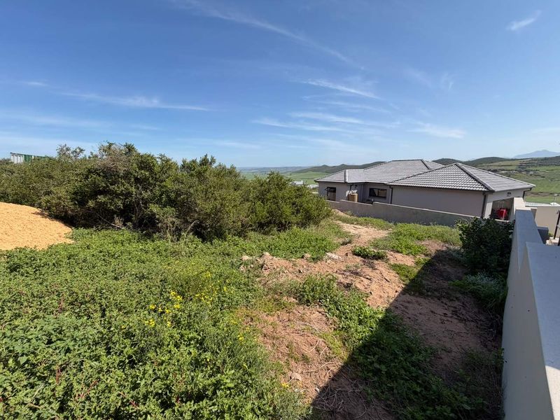 A view of the rear section of the vacant residential plot, featuring natural vegetation, boundary walling, and surrounding landscape views.
