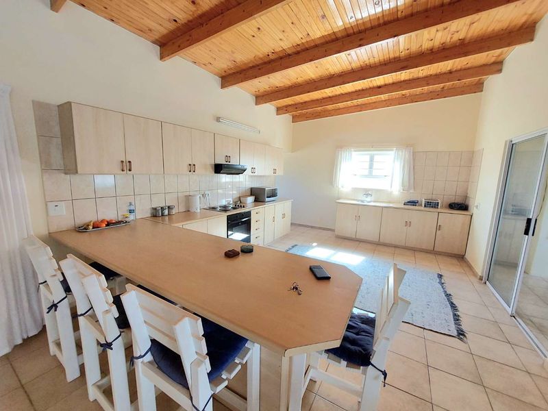 Spacious kitchen featuring light-toned cabinetry, laminate countertops, a built-in oven, and a distinctive exposed timber beam ceiling with tiled flooring throughout.