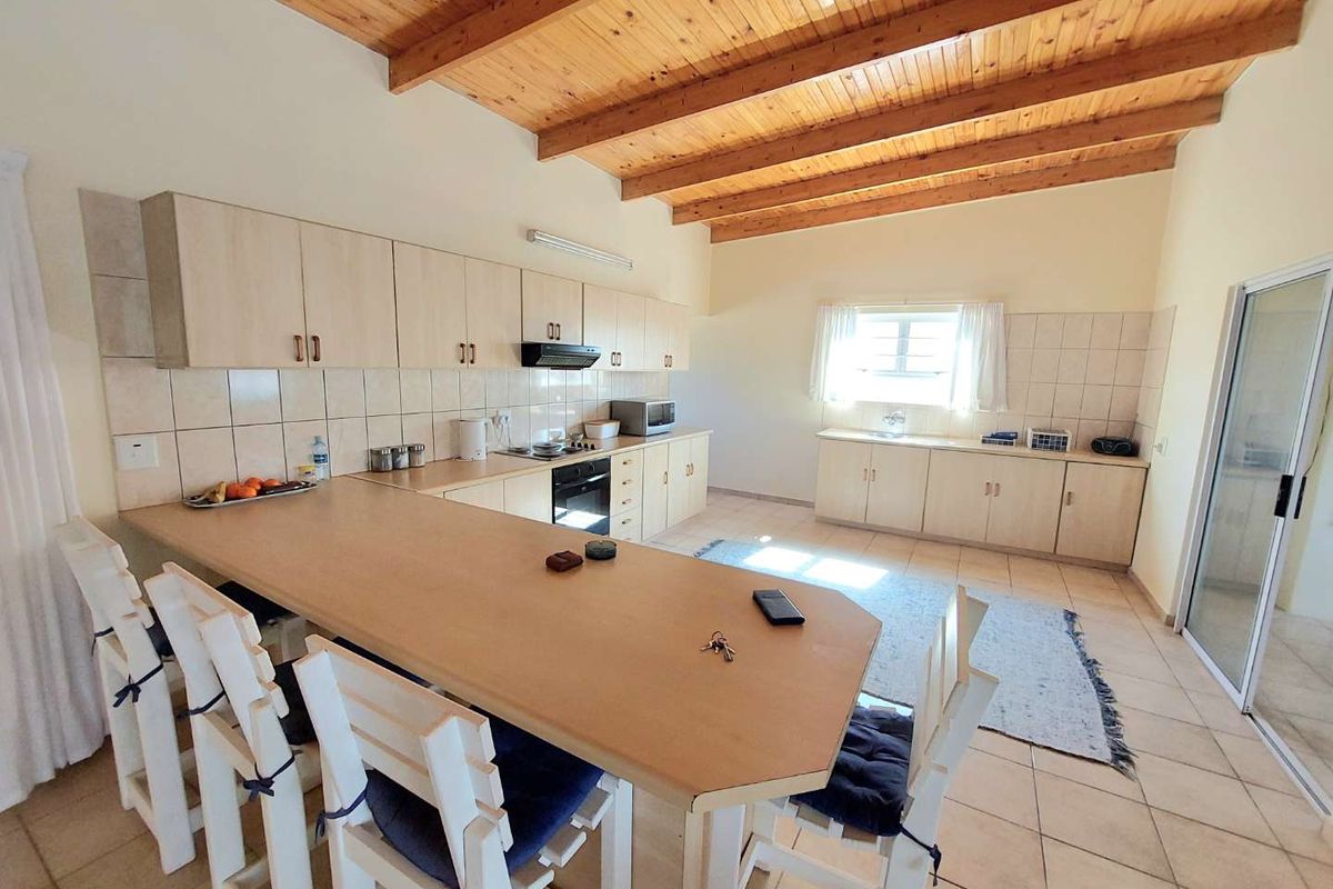 Spacious kitchen featuring light-toned cabinetry, laminate countertops, a built-in oven, and a distinctive exposed timber beam ceiling with tiled flooring throughout.