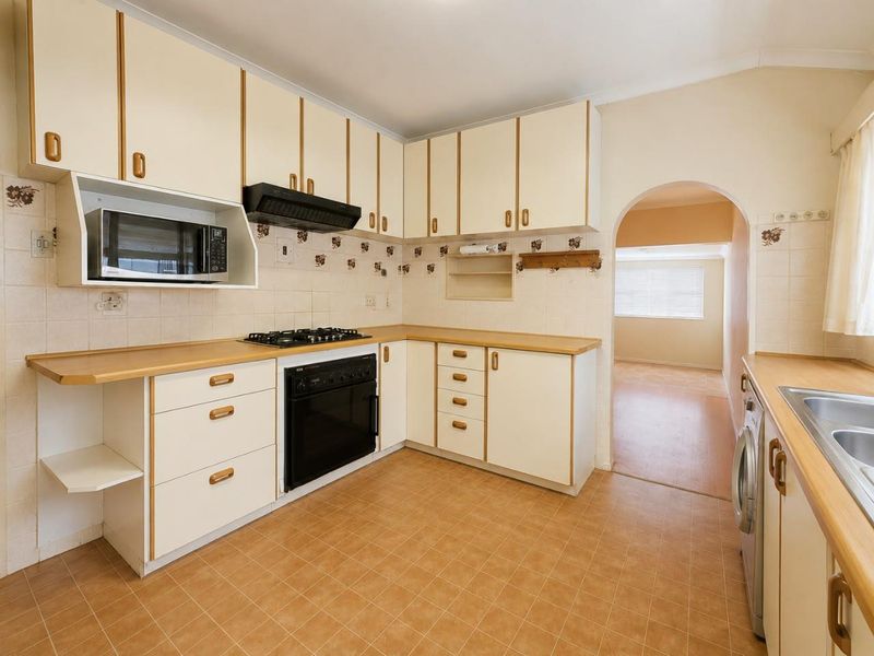 A functional kitchen featuring dated cabinetry, laminate countertops, a gas hob, built-in oven, and tiled backsplash, with an arched doorway leading to an adjacent room.