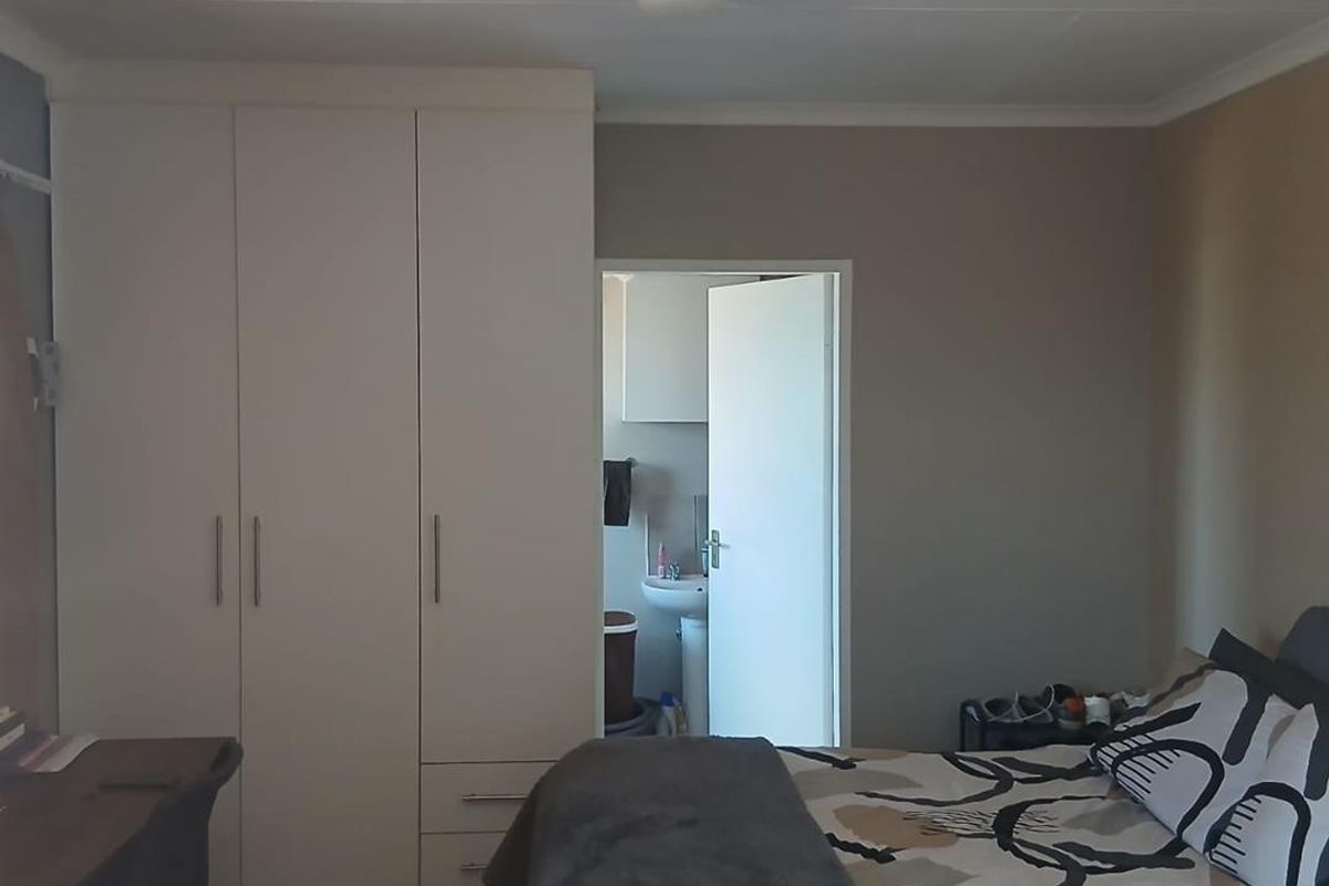 A bedroom featuring built-in cupboards and an adjoining en-suite bathroom with a basin.