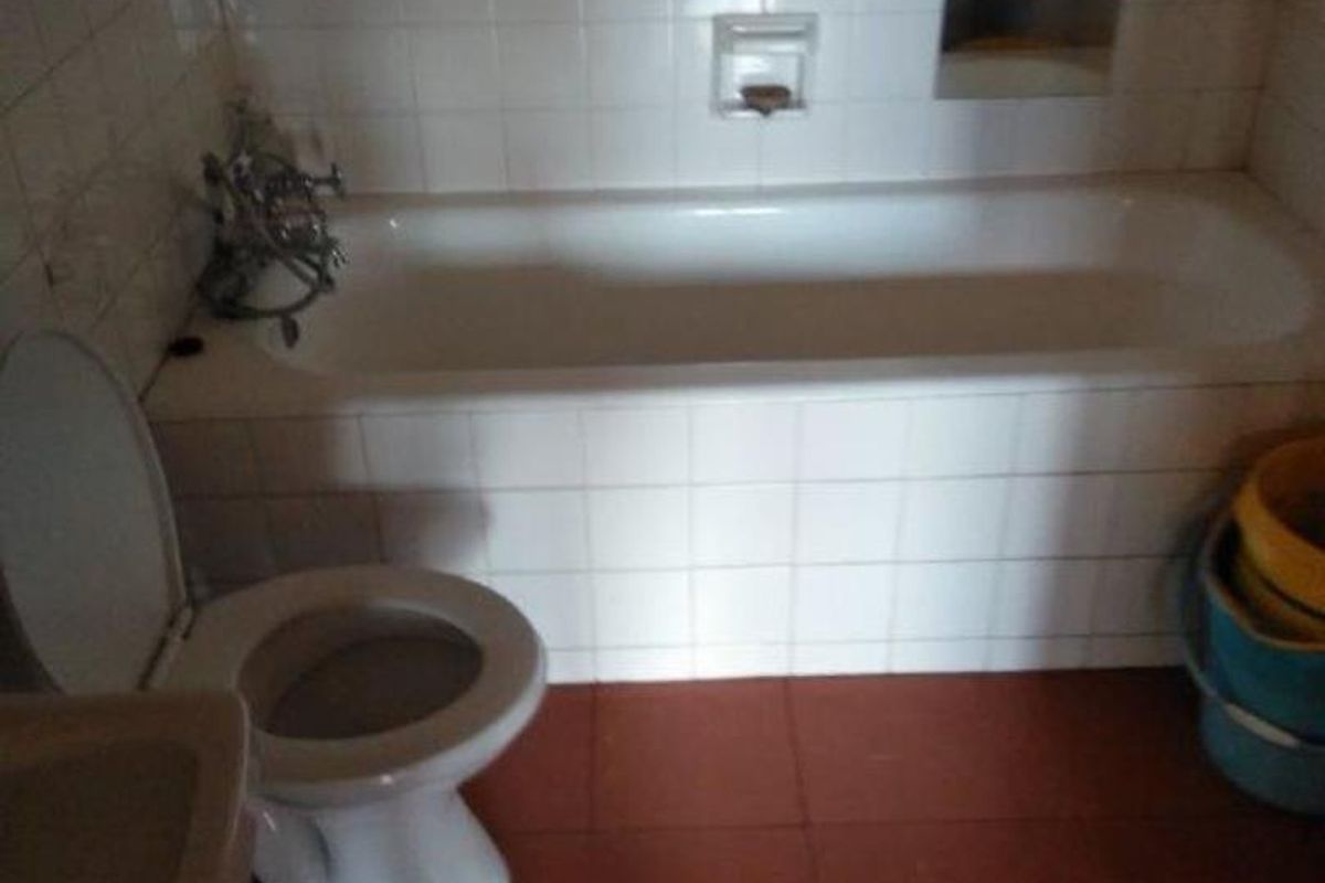A dated bathroom featuring a standard bathtub with tiled surround, a toilet, and tiled flooring, requiring modernization to improve functionality and aesthetic appeal.
