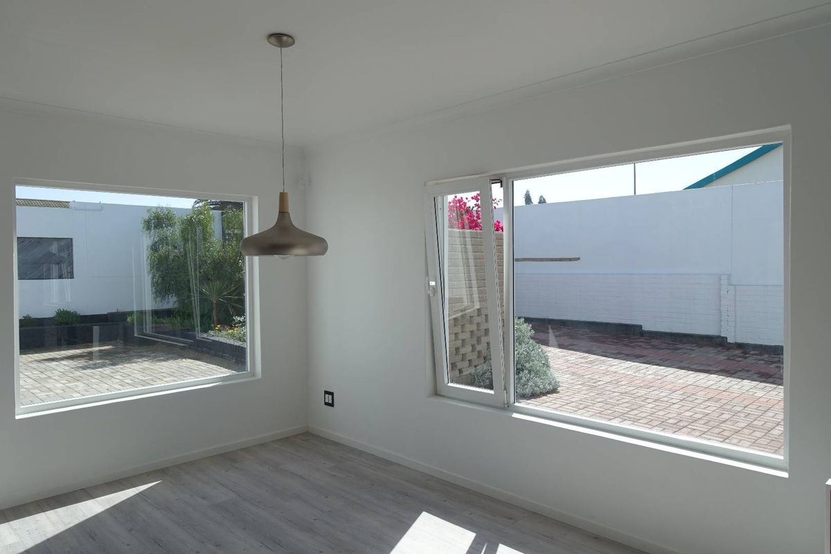 A bright, empty living space featuring modern laminate flooring, large windows with garden views, and a contemporary pendant light fixture.