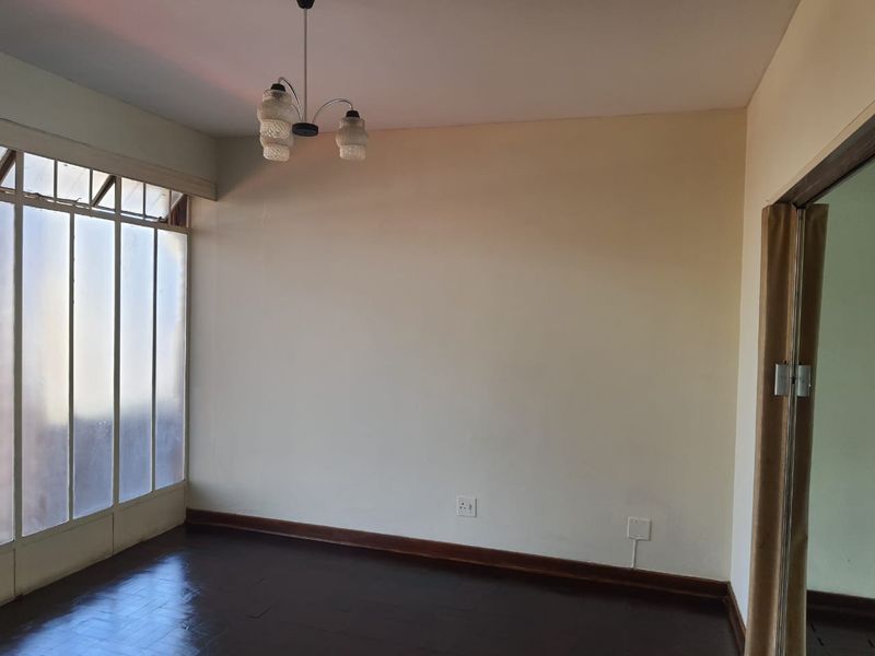 An empty living room featuring dark parquet flooring, neutral walls, and a large window, offering a blank canvas for interior design.
