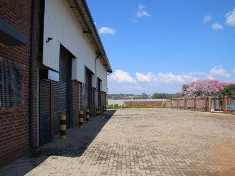 Industrial rear yard featuring multiple roller shutter doors, brick and metal facade, paved surface, and secure perimeter fencing.