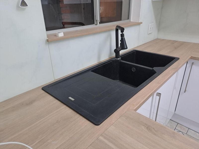 Modern kitchen area featuring a sleek double bowl composite sink with a contemporary gooseneck mixer tap set into a wood-look laminate countertop.