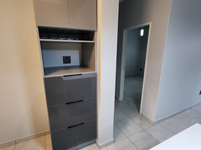 A clean, modern hallway featuring sleek grey built-in cabinetry and neutral tiled flooring, leading into an adjacent room.