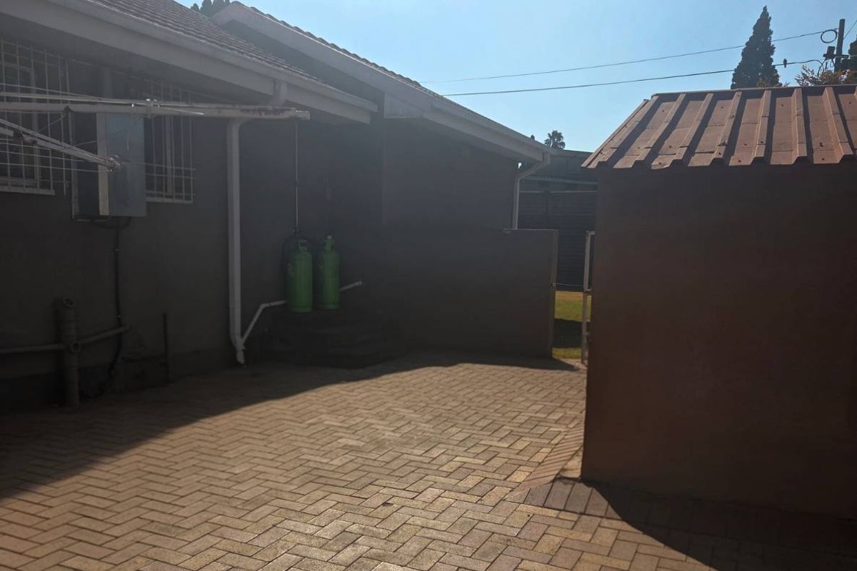 A paved rear courtyard area featuring a metal roof structure and exterior wall with security bars.