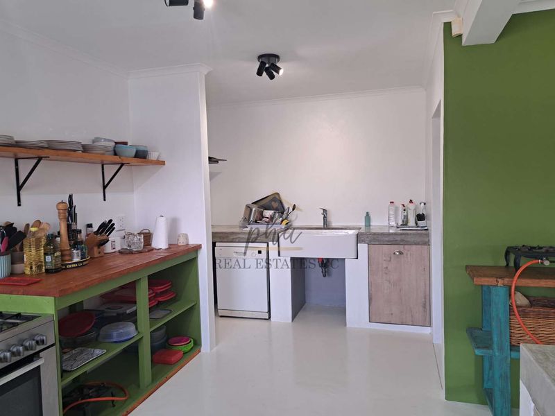 A functional kitchen area featuring a farmhouse sink, open shelving, and concrete countertops with a built-in oven.